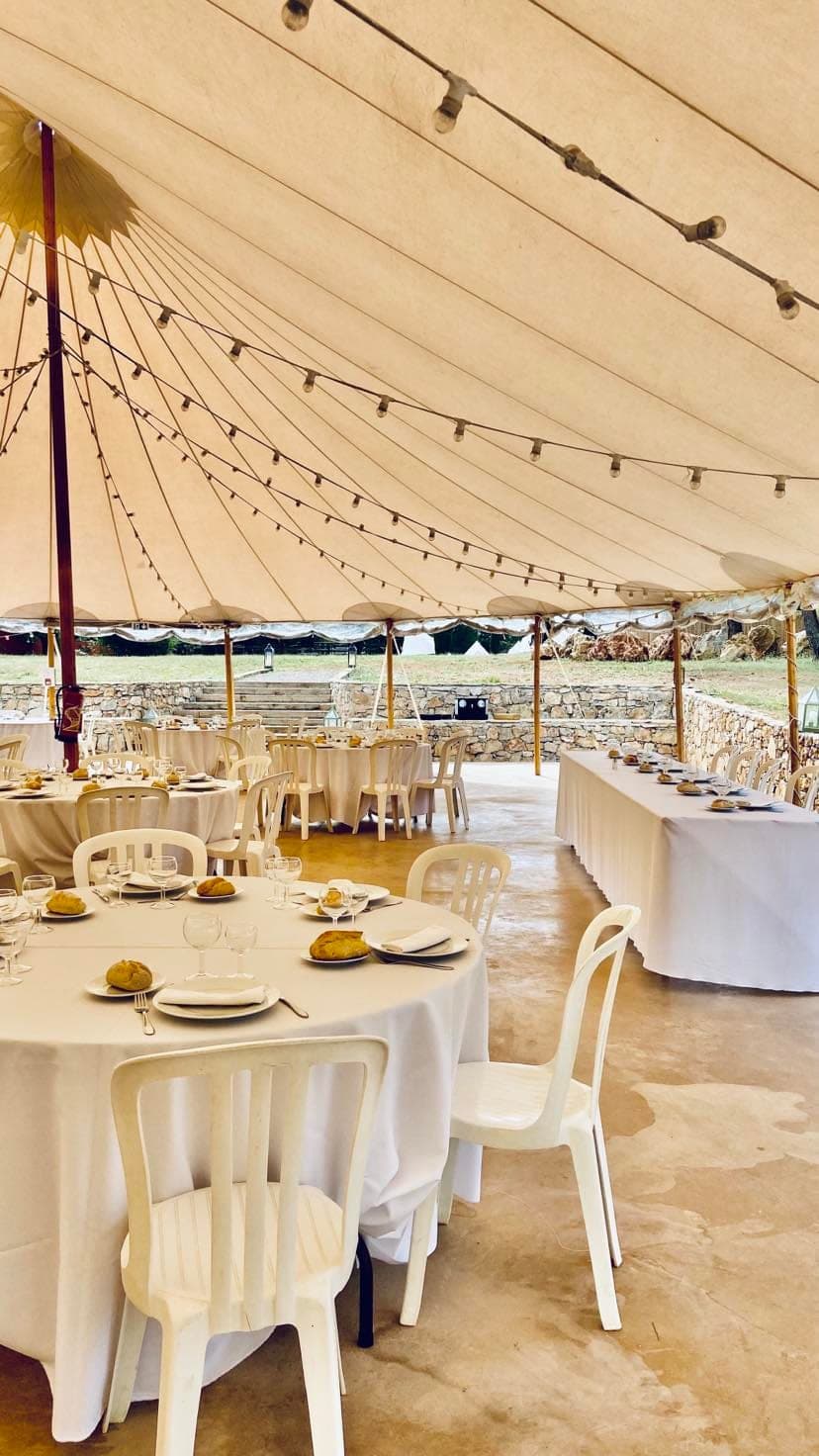 Intérieur d'une tente nomade : tables rondes dressées de blanc et guirlandes lumineuses sous la toile